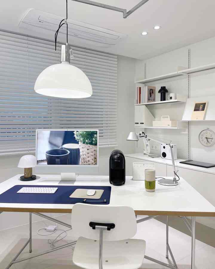 白とネイビートーンのホームオフィス、コンピュータデスクとスタンドライトが置かれた清潔感のある作業空間