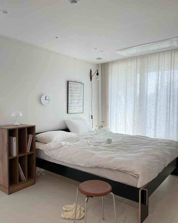 White and black toned bedroom featuring a black bed with white bedding and a wooden bookshelf, creating a calm modern atmosphere