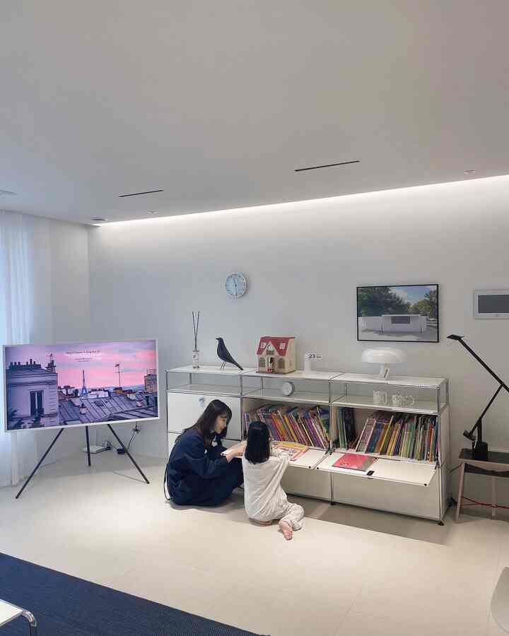 White-toned living room featuring a USM Haller bookshelf used for kids' books and as a desk, showcasing simple modern design