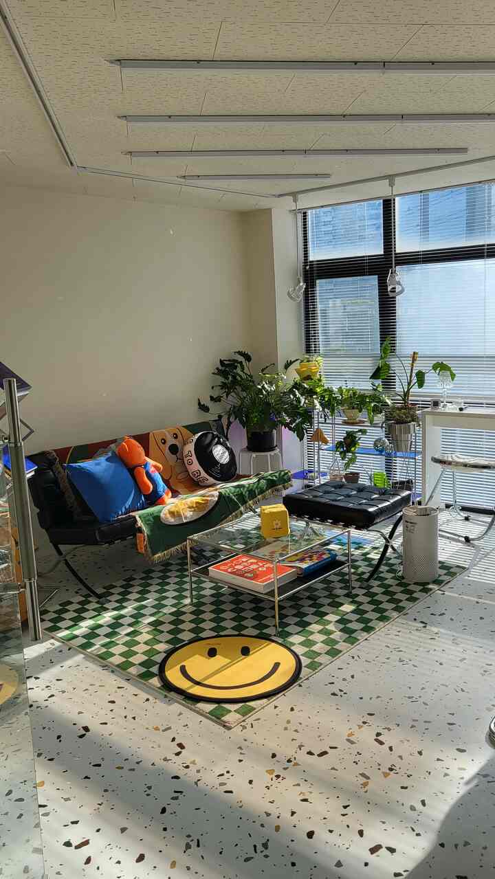 緑のチェック柄ラグとレトロな黒いソファ、多数の植物が配置された明るく快適なミッドセンチュリーモダンのホームオフィス空間