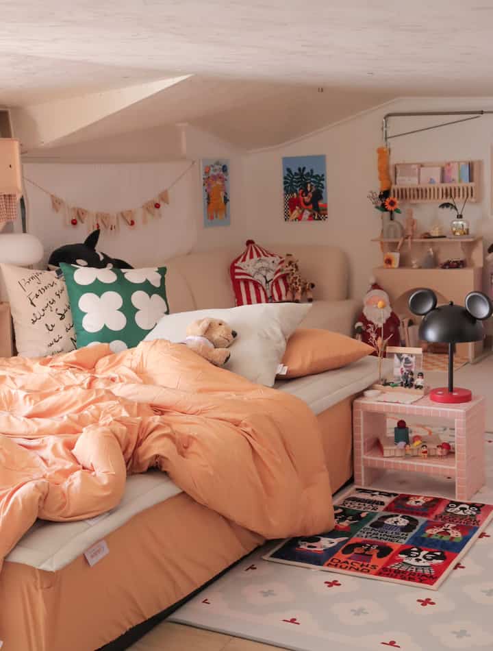 Warm beige and orange-toned loft bedroom featuring sofa, cushions, table lamp, and playful small decorative elements in cozy setting