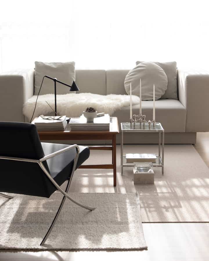 Bright beige-toned living room featuring cream sofa, black leather armchair, wooden table and layered rugs in a modern setting