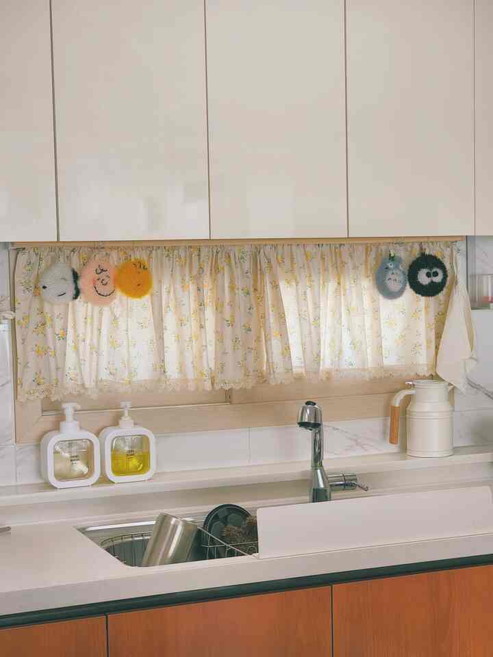 Bright white and natural wood-toned cozy kitchen featuring yellow floral valance curtain and cute Snoopy & Totoro scrubbing sponges