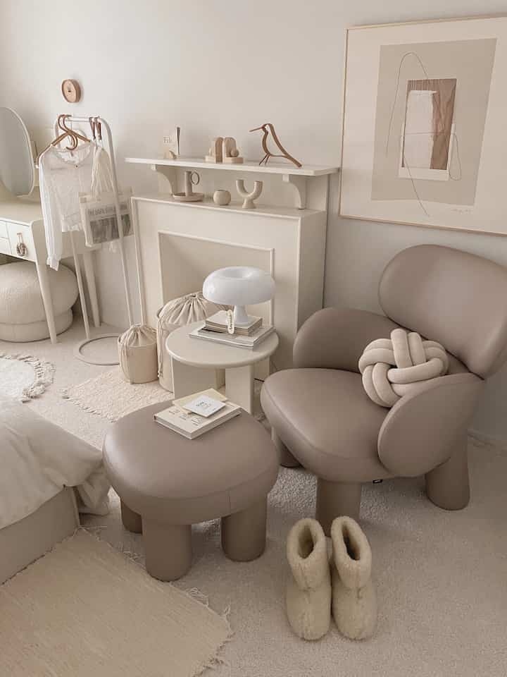 Natural beige toned living room featuring unique lounge armchair, matching stool, cozy rugs in a minimalist interior