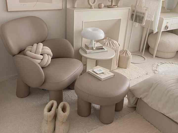Beige-toned bedroom space featuring soft-curved armchair and stool in a natural modern interior