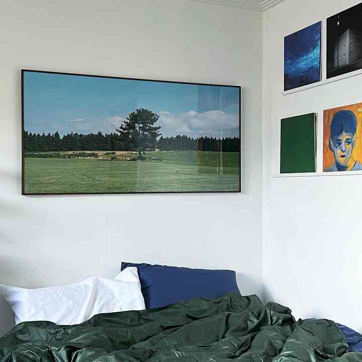 白い壁にネイビーとグリーンの寝具が配置され、壁にはポスターと額縁が並ぶ、すっきりとした寝室のインテリア