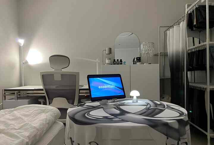 White and gray toned studio bedroom and home office space featuring a compact bed, desk, office chair, and open wardrobe in a modern interior