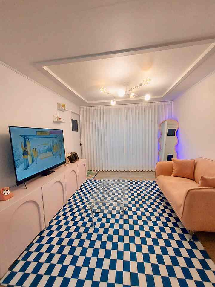 ピンクと青のアクセントが映えるミッドセンチュリーモダンのリビング、透明なテーブルと変形ミラーが配置された雰囲気のある空間