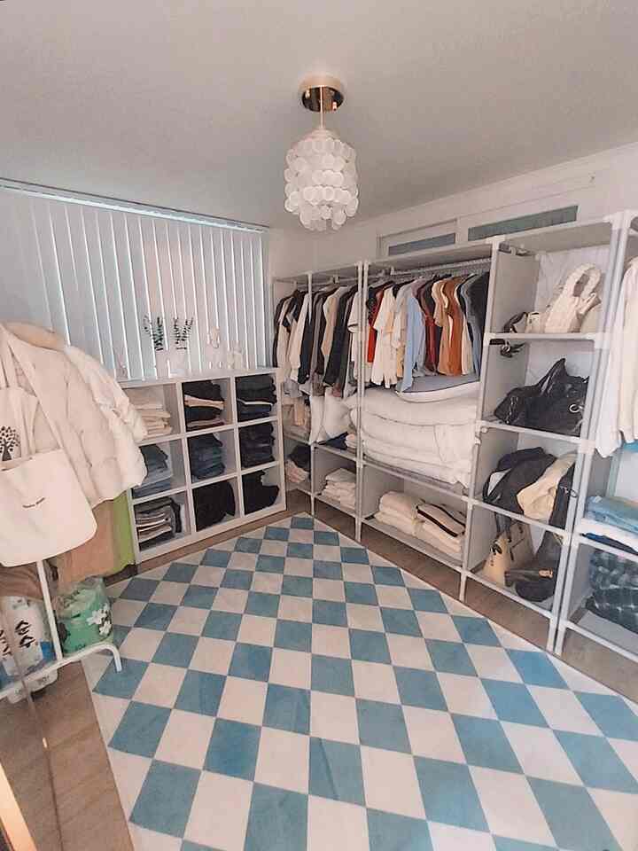 白と青の色調のウォークインクローゼット、貝殻のシャンデリアとシステムラック、チェック柄ラグがある清潔感のある収納空間