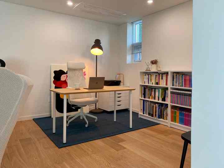 Clean study space blending white and wood tones, featuring a blue rug and bookshelf creating a cozy home office vibe