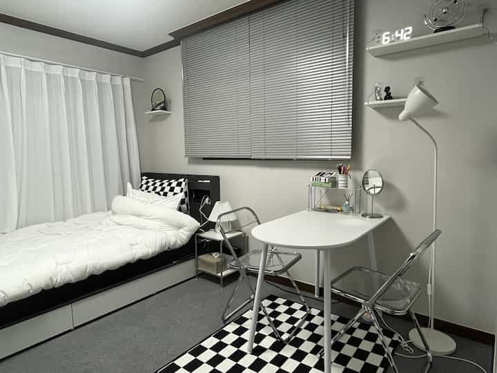 白とグレーのトーンのワンルーム寝室、コンパクトな机とベッドが配置されたミニマルで清潔感のある空間