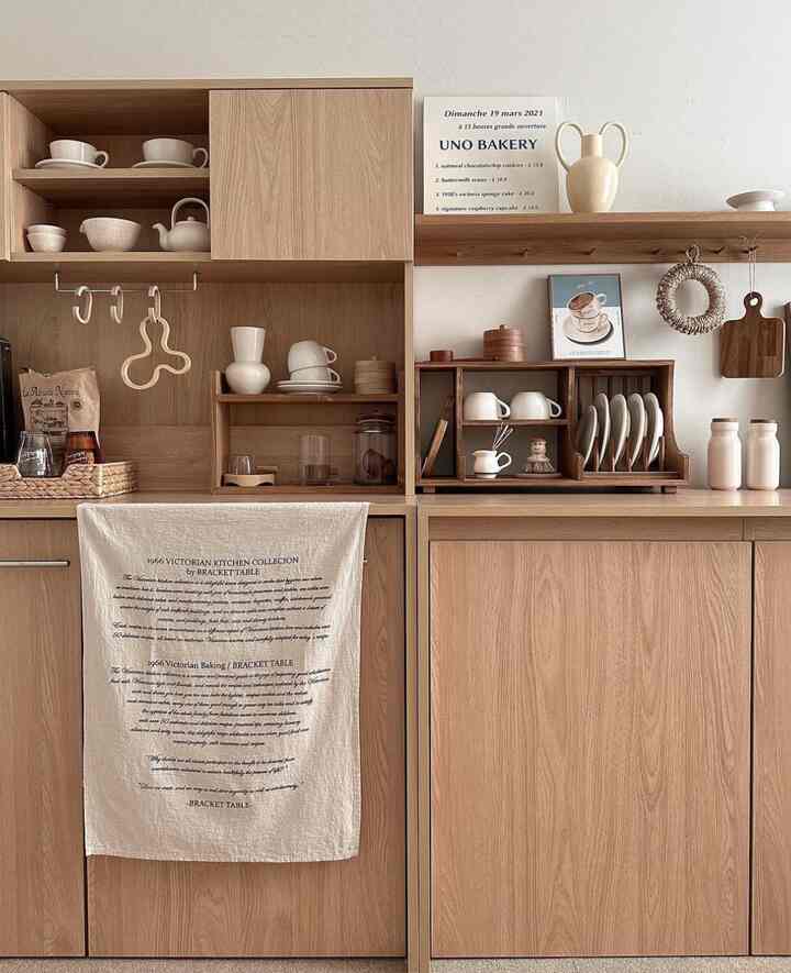Natural wood tone kitchen space featuring wall shelves, picture frame, and vases with warm atmosphere