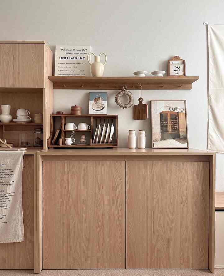 Natural wood tone kitchen space featuring minimal storage, teacups, and picture frames with a cozy atmosphere