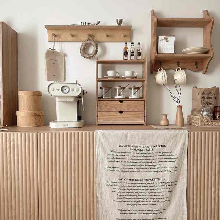 Natural wood tone kitchen space featuring a cream coffee machine, wooden shelves with coffee cups and jars, creating a cozy home cafe atmosphere