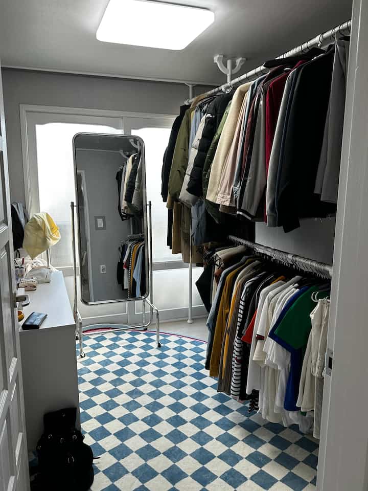 White and blue toned walk-in closet featuring clothing racks, full-length mirror, and checkerboard rug in a tidy space