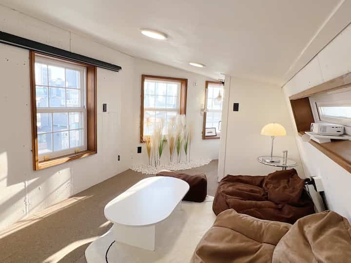 Ivory walls and beige flooring natural style living room featuring reed plants, brown bean bag sofa, and white coffee table with warm, calm atmosphere