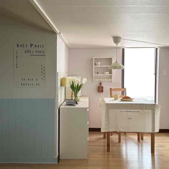 白と木目調が調和したキッチン、フレンチ文字入りのテーブルクロスと花瓶が温かみのある雰囲気を醸し出すインテリア