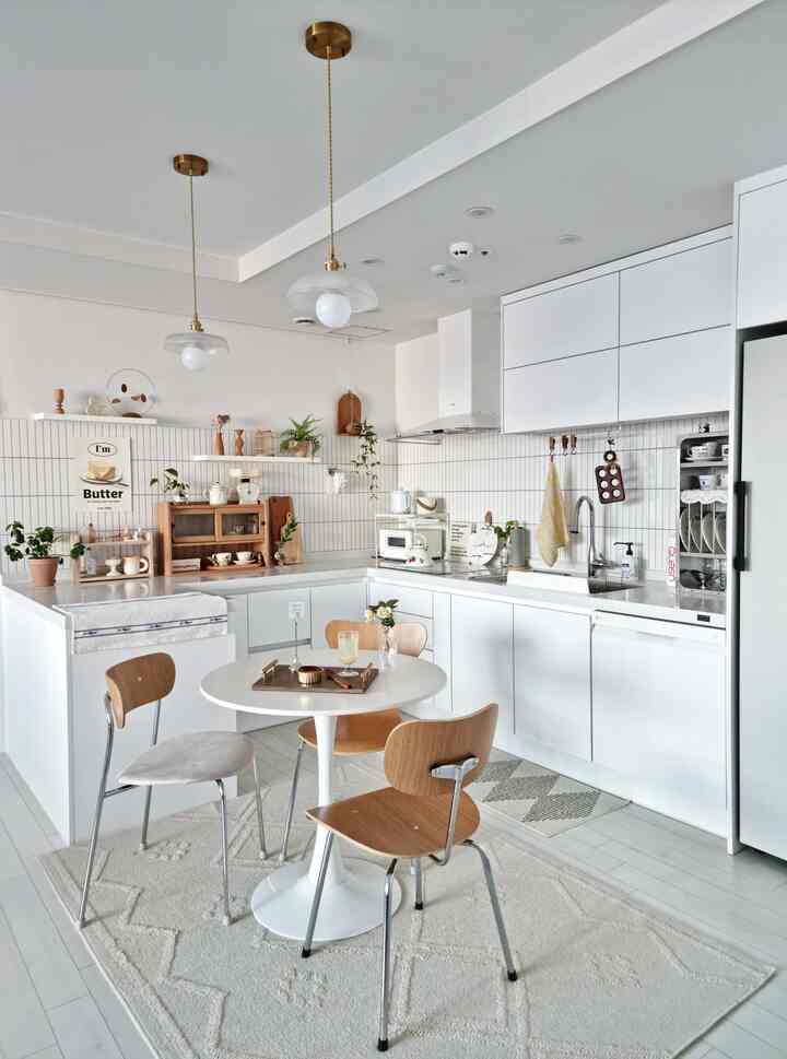Bright white-toned kitchen space featuring a round dining table with wood-tone chairs in a cozy interior
