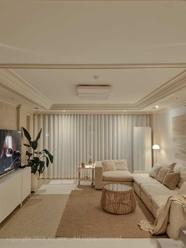 Natural-toned living room featuring a modular sofa, curtains, and rattan coffee table with cozy ambiance