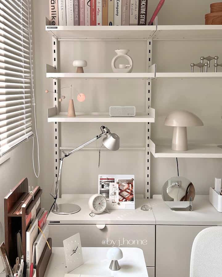 White and silver toned home office space featuring desk, shelves, and table lamps with a clean modern atmosphere
