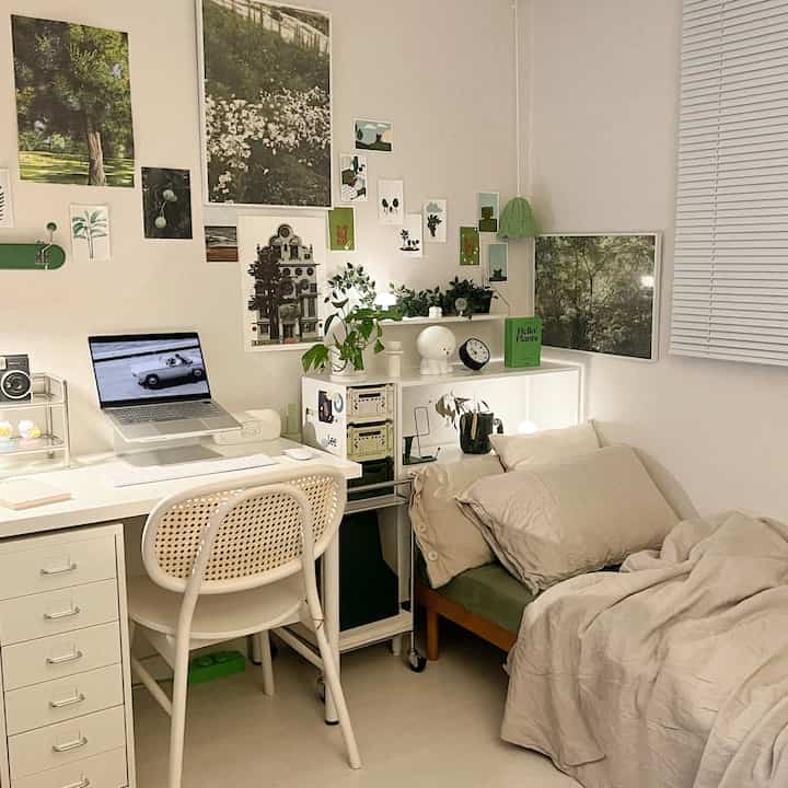 A cozy bedroom in white and beige tones, featuring a desk, chair, various plants, and framed wall art elegantly arranged