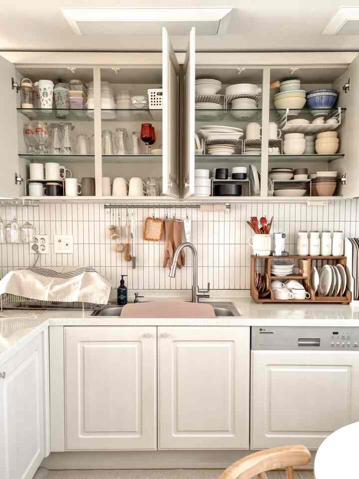 白とナチュラルカラーのキッチン、上部の収納棚に皿とボウルが整然と並んだ雰囲気のあるインテリア