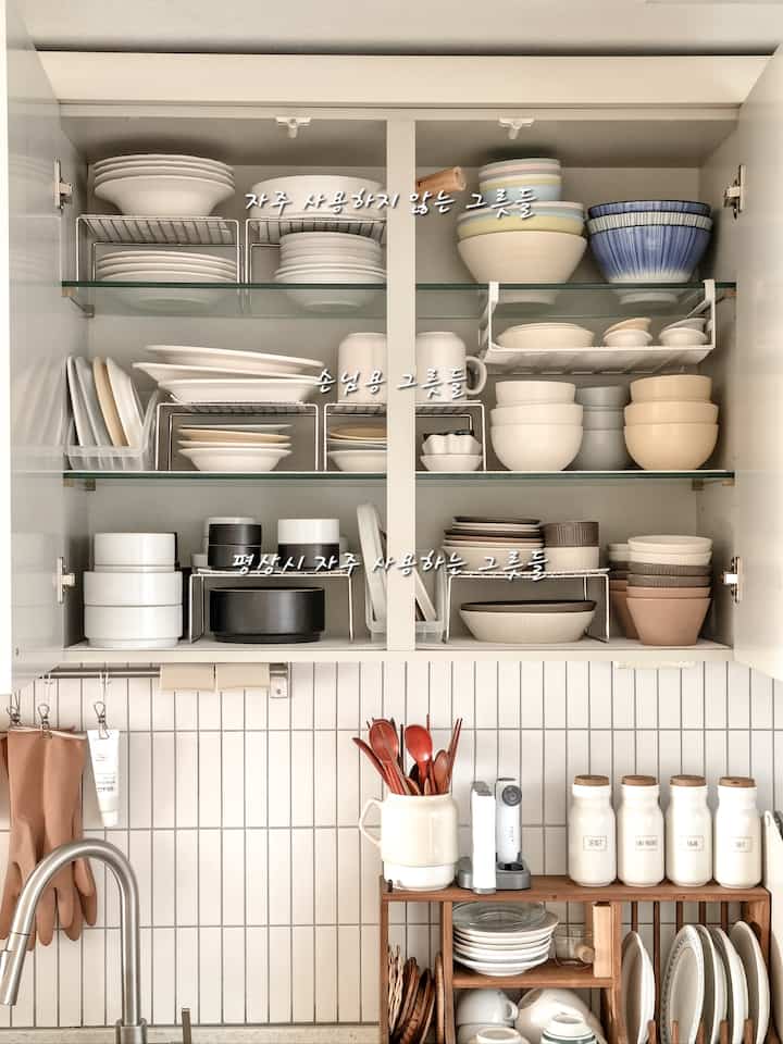 白と木目調が調和したキッチンの上部収納、多様な皿とボウルが整頓された収納スペース