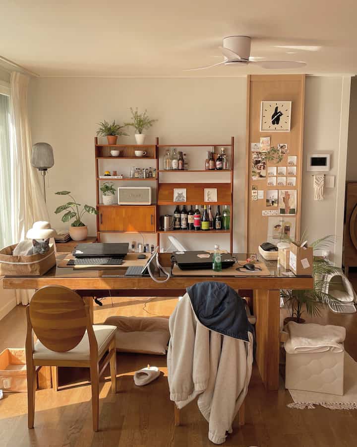 Cozy living room with warm sunlight, wooden table set up for remote work, and a cat lounging in a basket