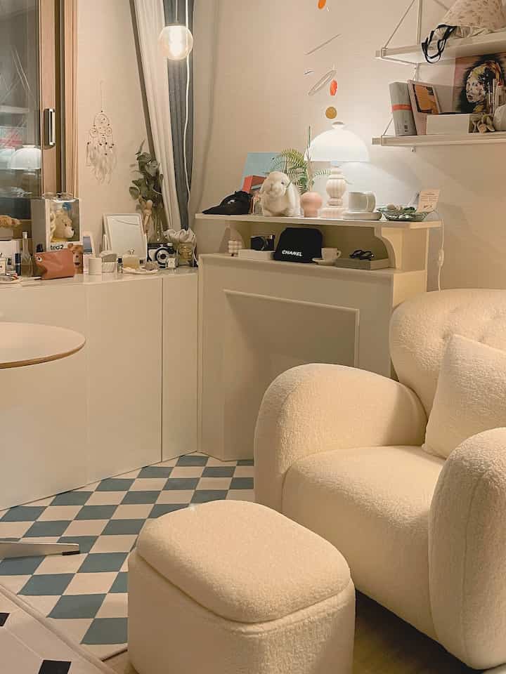 Beige and white toned living room featuring a soft armchair with ottoman and checked patterned rug creating a cozy cafe style atmosphere