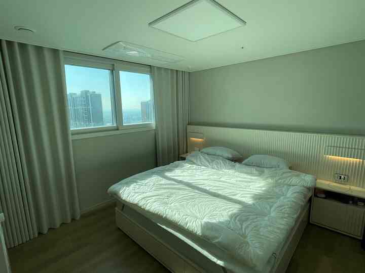 白とベージュ調の寝室、収納ベッドフレームと遮光カーテンが配置されたシンプルでホテルライクなインテリア