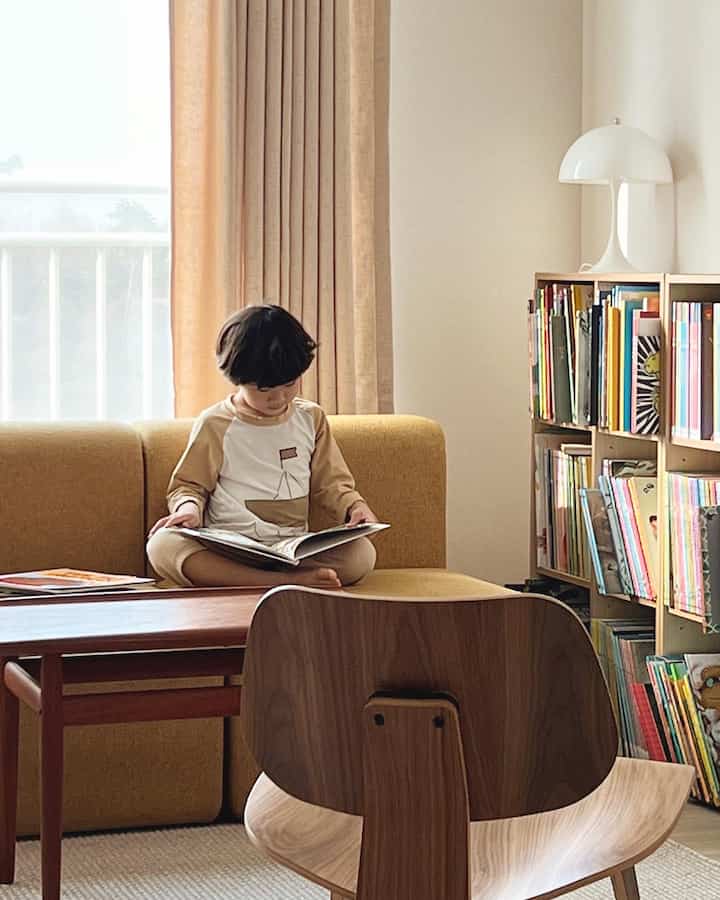 Yellow and wood-tone kids' room featuring a child reading a book on a sofa with a calm atmosphere