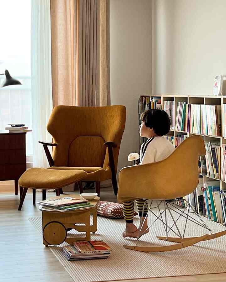 暖かいマスタード色のアームチェアとロッキングチェアが配置されたナチュラルトーンの子供部屋、子供がくつろいで座っている空間