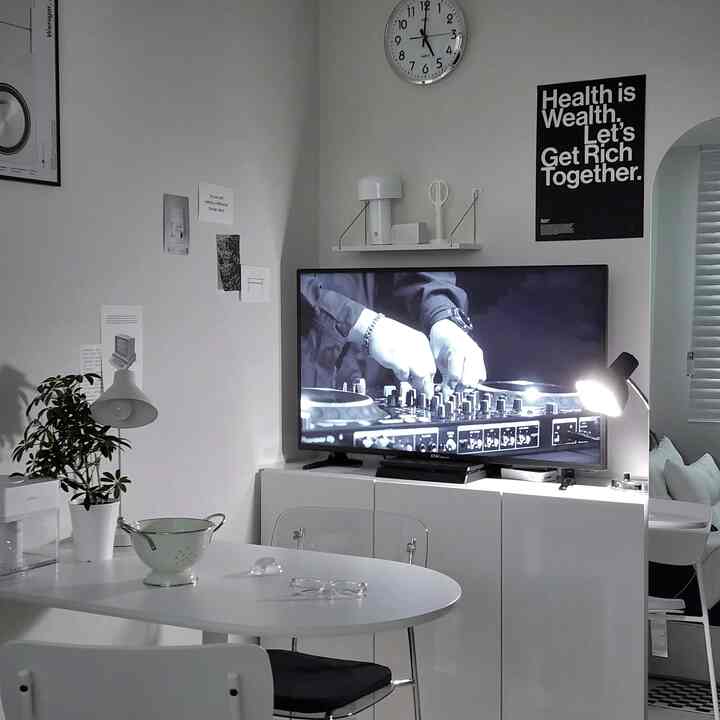 モノトーンのリビング、白いダイニングテーブルと植物、テレビ台の上にテーブルランプが配置されたシンプルなインテリア