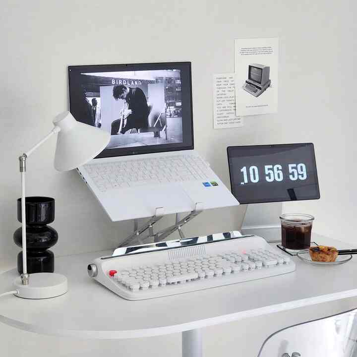 Bright, clean white-toned home office space featuring white mechanical keyboard and laptop on stand on a simple desk