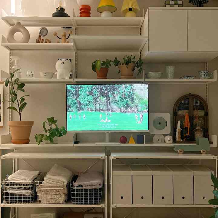White and natural toned living room storage area with organized baskets and plants, featuring clean interior style