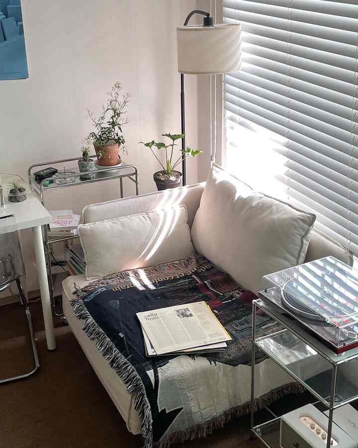 ナチュラルなホワイトトーンのリビング、白いソファとメタルシェルフ、ブラインドが配置された雰囲気のあるインテリア