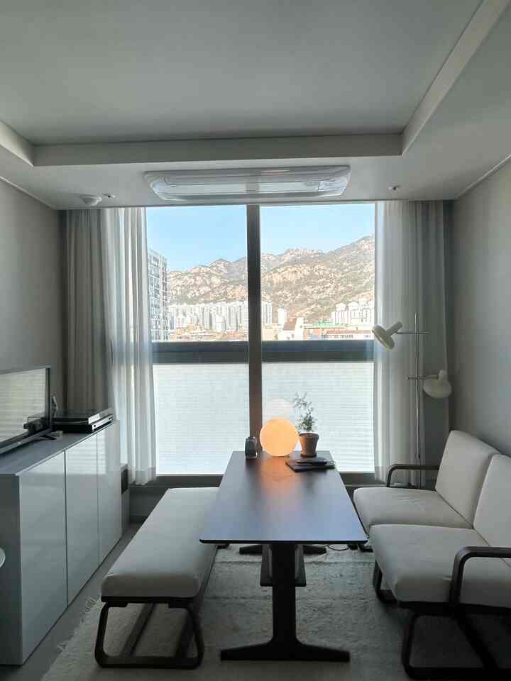 Natural modern dining room in white and brown tones, featuring a modern sofa, dining table, and large window with city view