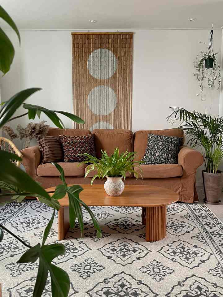 Natural tone living room with wood table, brown sofa, patterned carpet, and multiple plants arranged neatly