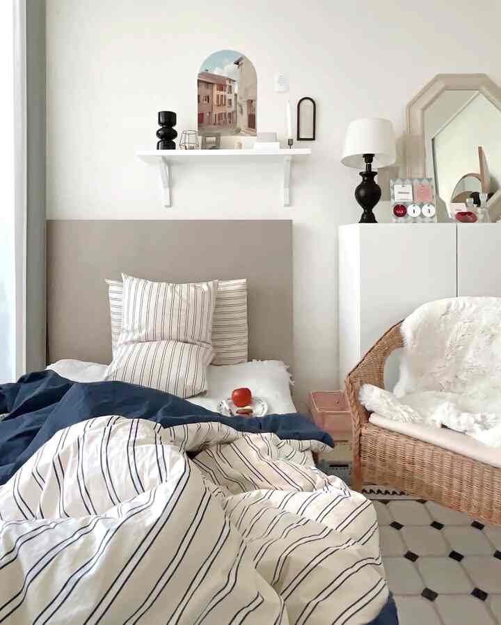 ベージュとネイビーのトーンの寝室、ストライプの寝具とラタンチェアが調和した雰囲気のあるインテリア