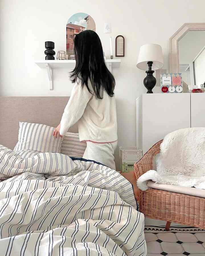 A cozy bedroom in white and beige tones featuring striped bedding and a rattan armchair in a natural modern style