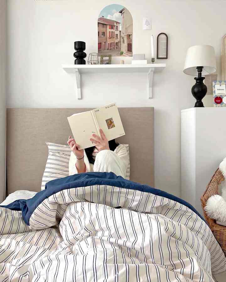 Navy and white toned bedroom featuring a bed with striped duvet cover and pillows, and a rattan armchair creating a cozy atmosphere