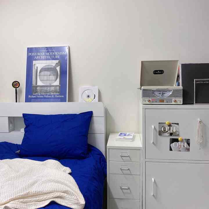 Modern bedroom with white walls and furniture, featuring deep blue bedding, nightstand, and a retro turntable creating a cozy vibe