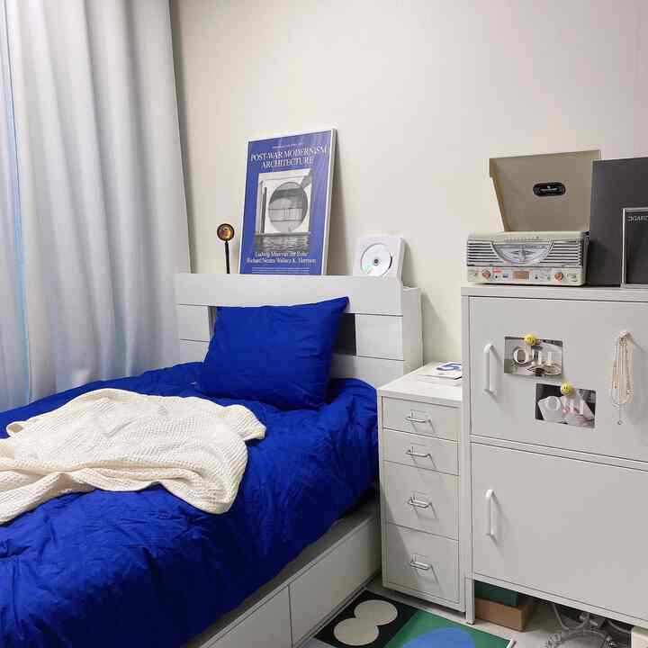 Cozy single bedroom with white walls and furniture, featuring deep blue bedding and integrated storage