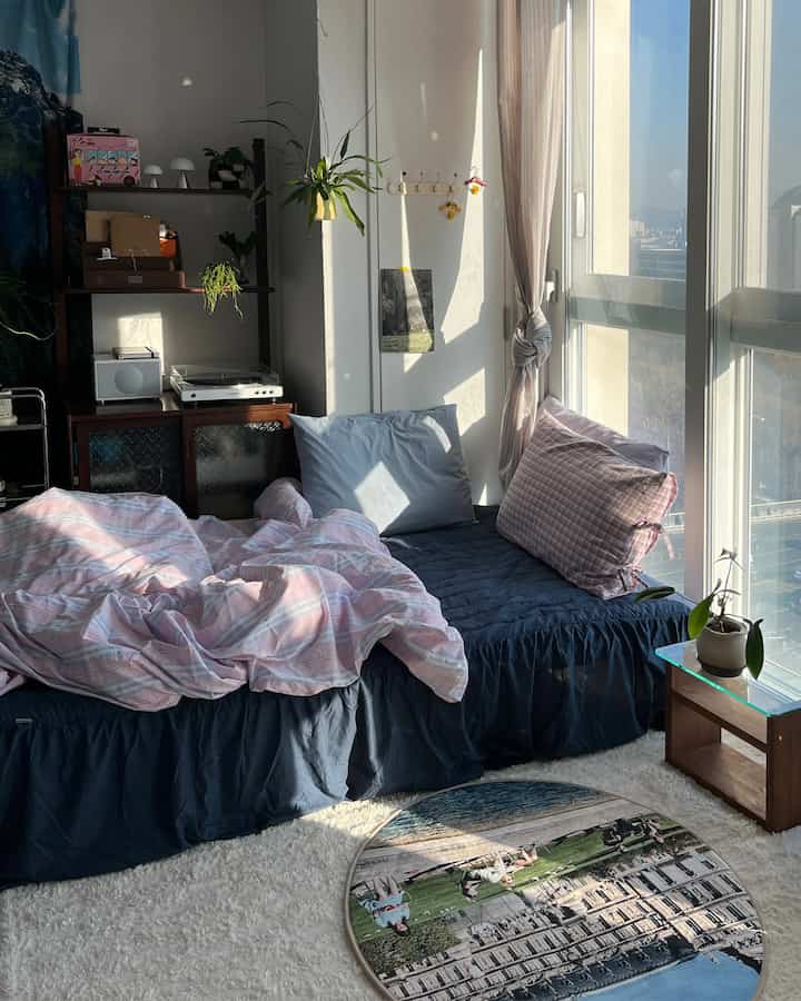 白とネイビーのトーンのワンルーム寝室、寝具とラグが配置された自然で落ち着いた雰囲気のある空間