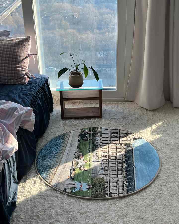 Cozy studio bedroom with navy bedding and a soft rug, featuring natural light and a small plant by the glass table