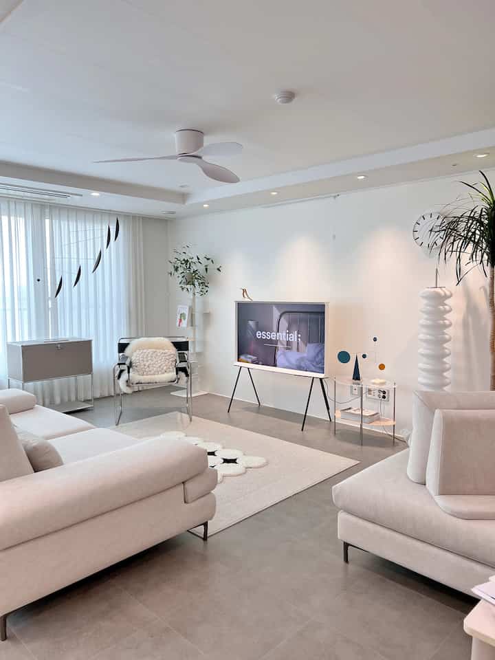 白を基調としたリビング、ミッドセンチュリーモダンのソファとアームチェア、モビール、シーリングファンが配置された印象的な空間