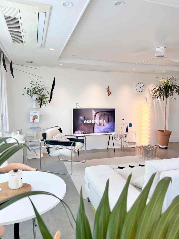 Bright white-toned living room featuring a sofa, armchair, wall-mounted TV, and floor lamp creating a cozy atmosphere