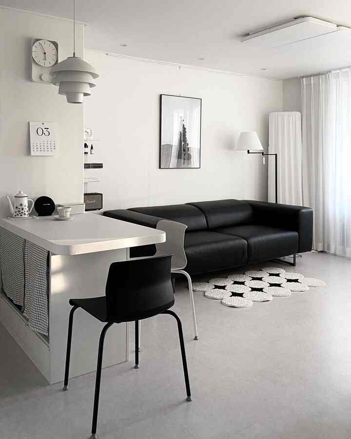 Modern living room in white and black tones featuring a black sofa, white dining chairs, and a floor lamp in a simple setting