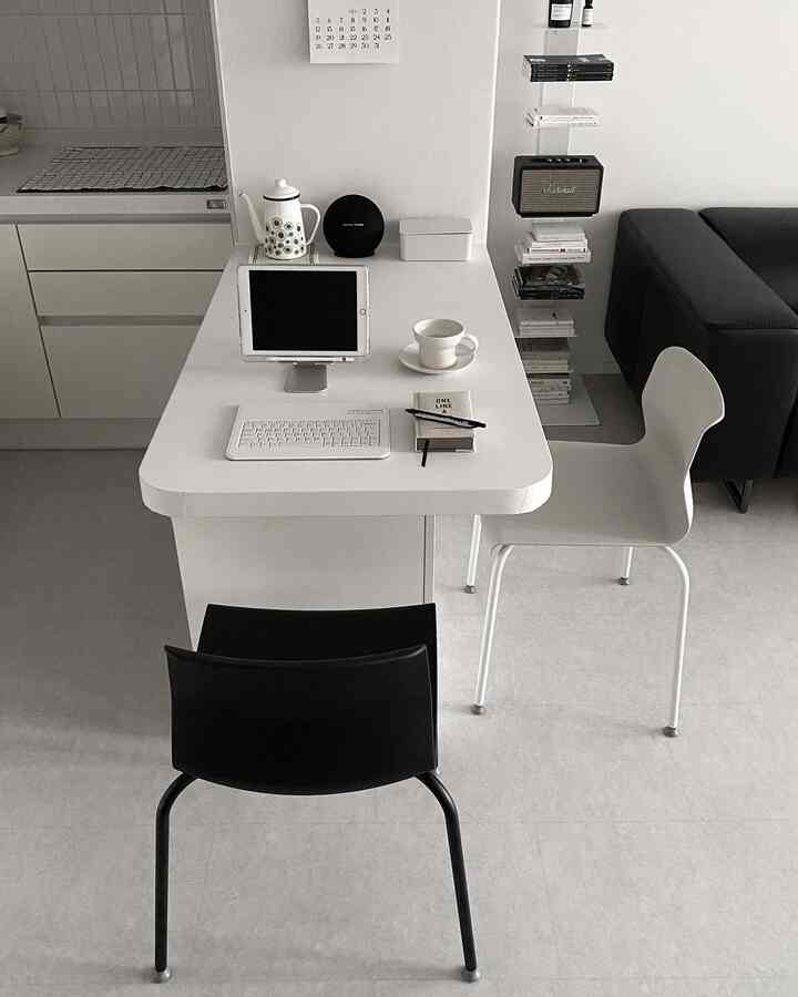 Modern living room and kitchen space in white and black tones featuring a workspace table and chairs for remote work