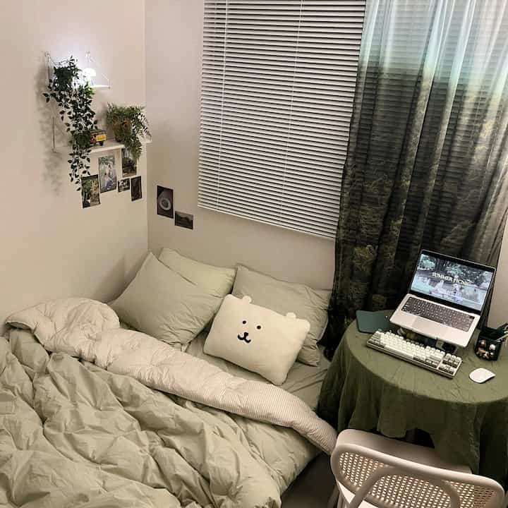 柔らかなベージュとオリーブグリーンの色調の狭い寝室、マットレスとかわいいクッション、ノートパソコンが置かれた丸テーブルが配置された居心地の良い空間